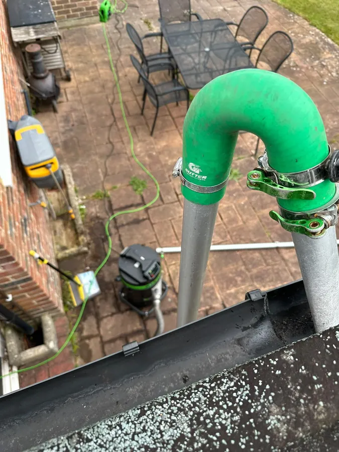 Gutter vacuum hose reaching down from the roofline above a patio